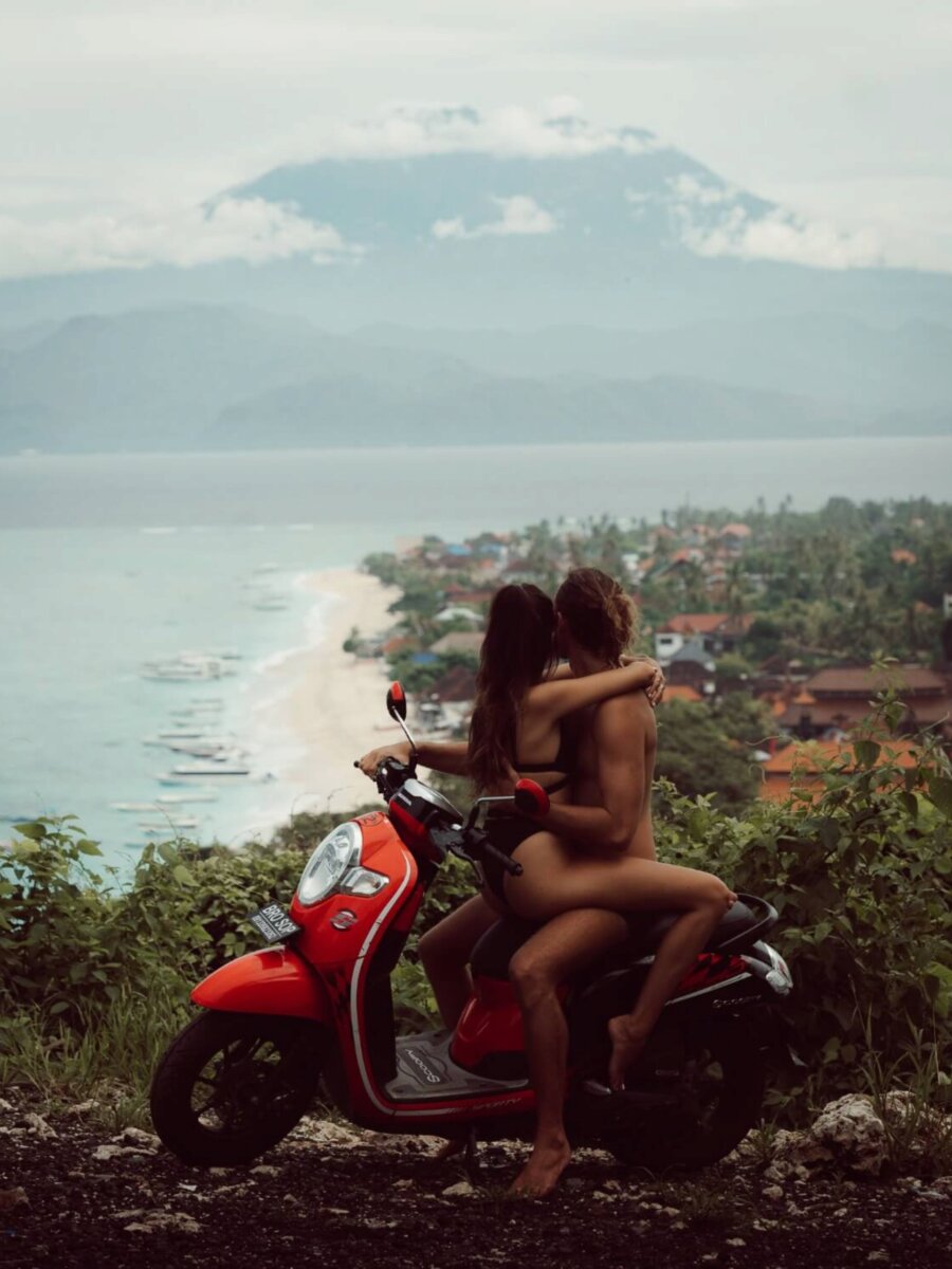 couple sitting on a red scooter with a volcano in the bakc